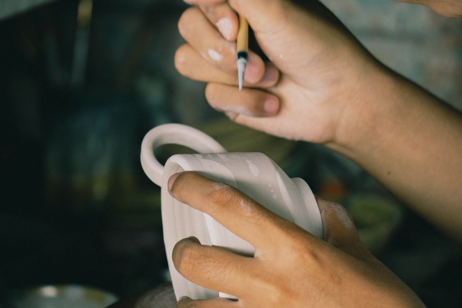 Artisan painting intricate designs on ceramic pottery in a close-up shot.