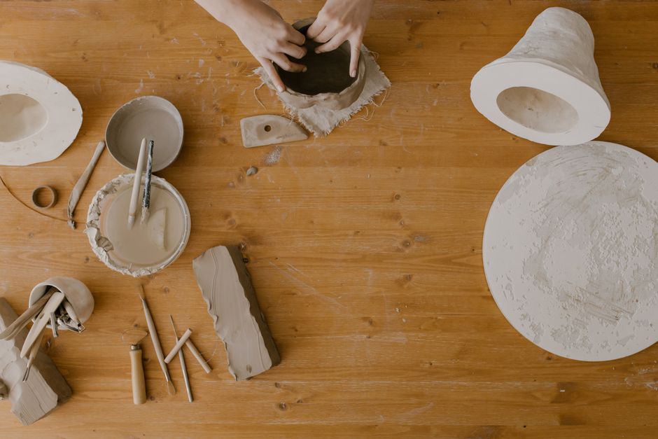Hands sculpting clay in a pottery workshop, captured from above on a wooden table.