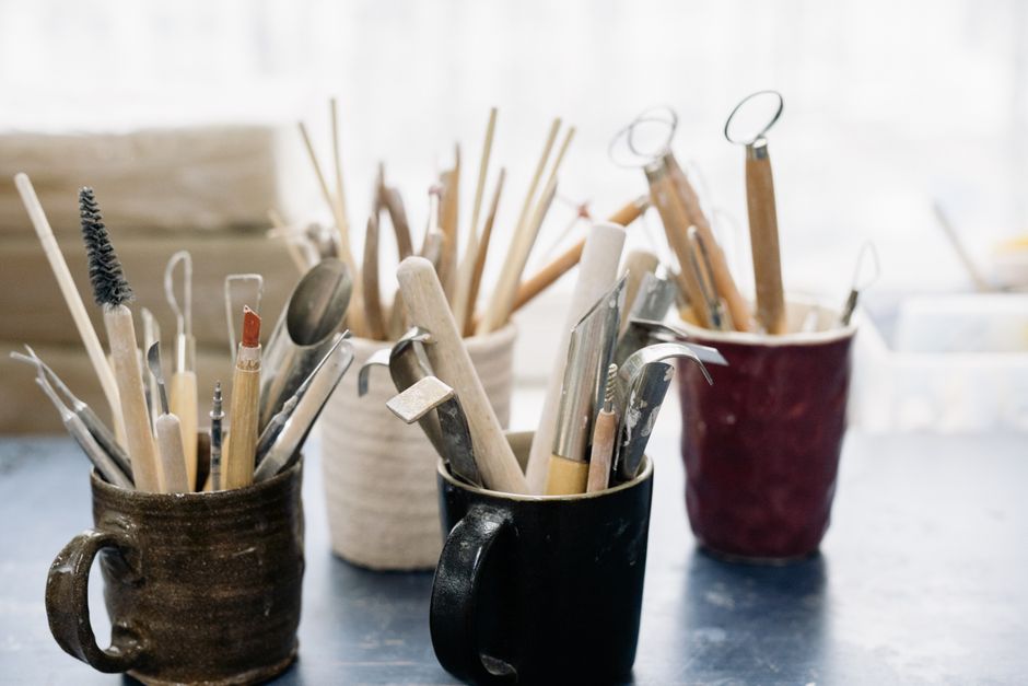 A collection of pottery tools in mugs on a workshop table, perfect for crafting enthusiasts.