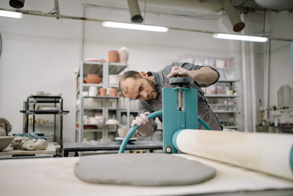 Artist using a slab roller for pottery in a studio environment, focusing on creativity and craftsmanship.