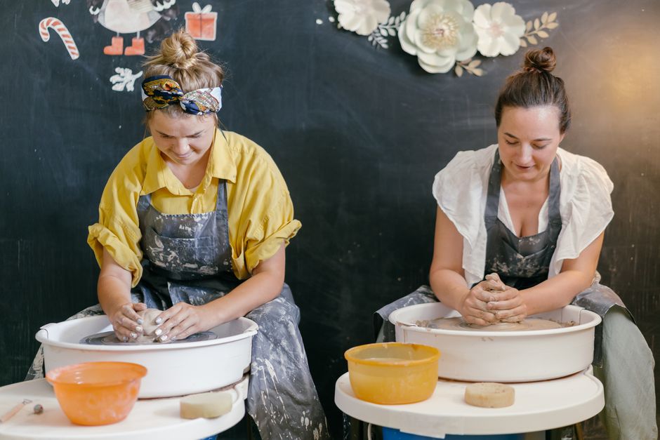 Two women working with clay on pottery wheels in a cozy studio setting.